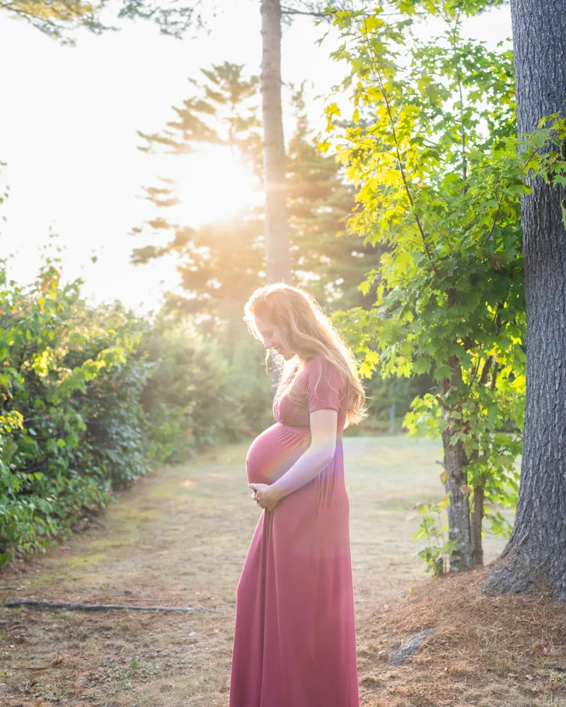 An expectant couple in a sunlit field holding a strip of ultrasound photos.