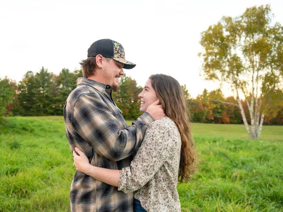 A couple embracing in front of a weathered grey barn.