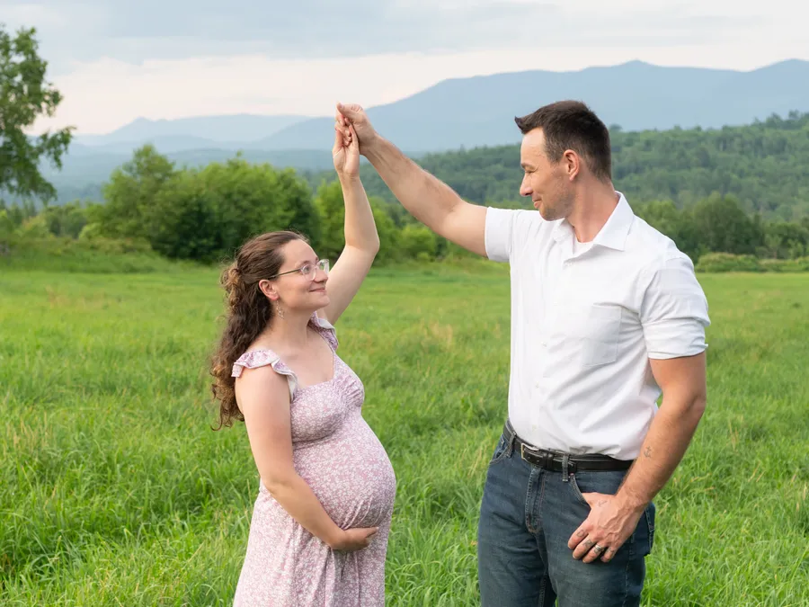 An expecting couple holding an ultrasound photo in a field.